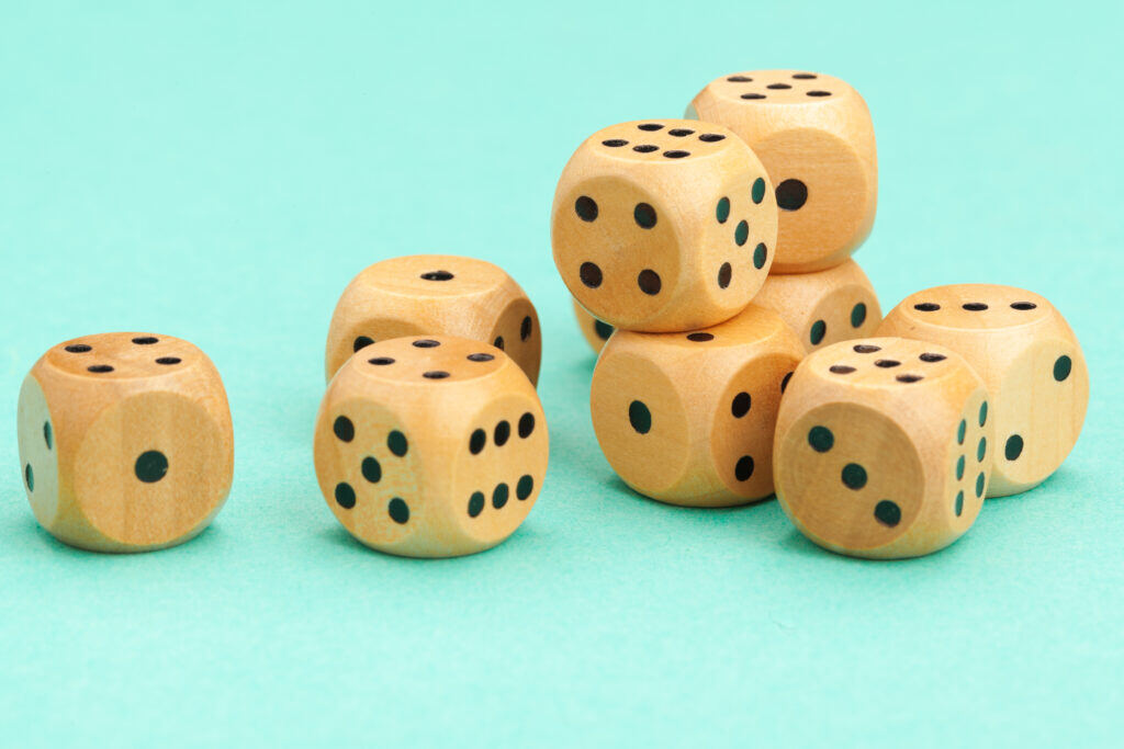 Wooden gaming dice with black markings rest against a robin's-egg blue background. The image accompanies a blog post about how a world without assessments would mean talent decisions are made randomly, as if decision-makers were rolling the dice on candidates.
